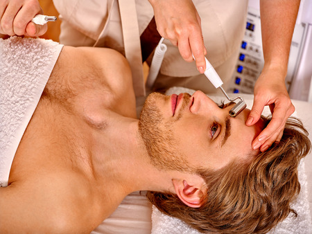 Young man looking up receiving electric galvanic face spa massage at beauty salon.の写真素材