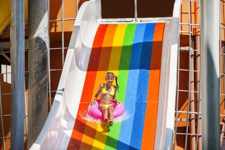 Female kid on water slide at aquapark. Summer holiday.