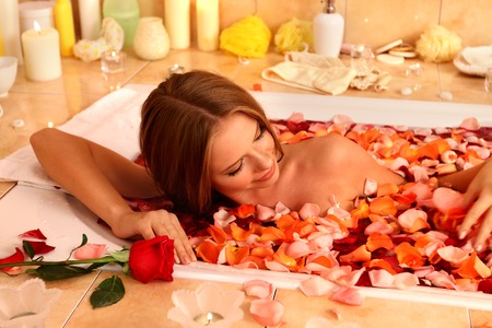 Young beautiful woman luxuriating with rose petals hot bath in spa saloon.