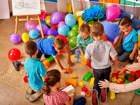 Group children game blocks on floor in kindergarten . Balloons on floor Top view.