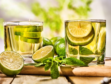Alcohol drink. Wooden boards with alcohol green cocktail drink glasses and half lime .Drink number twenty three cocktail mojito with slice lime and mint leaf. Country life outdoor. Light background.の写真素材