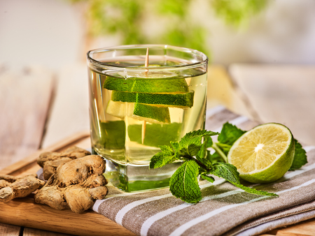 Healthy detox drink with ginger . On wooden boards glass with lime green tea and mint. A mint ginger drink number twenty seven with half and slice lime and napkin. Country life. Light background.の写真素材