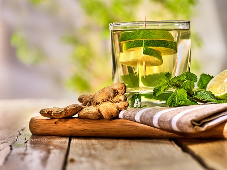 Healthy detox drink with ginger . On wooden boards glass with lime green tea and mint. A healthy mint ginger drink number twenty eight with half slice lime and napkin. Country life. Light background.の写真素材