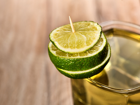 Alcohol drink. On wooden boards is glass with alcohol green transparent drink. A drink number five cocktail part of glass decorated with slice of lime. Country life. Light background.の写真素材