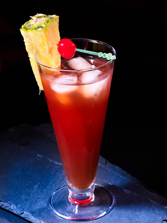 Cold red cocktail drink in highball glass decoration pineapple cherry. Cocktail card . Dark background.の写真素材
