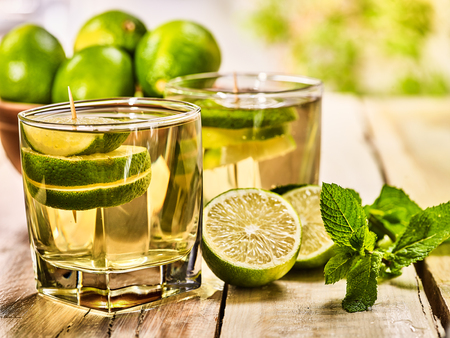 Country drink. On wooden boards are two glasses with green transparent drink and lime glue bowl. A drink number nineteen mojito with mint leaf on sunlight . Country life. Light background.の写真素材