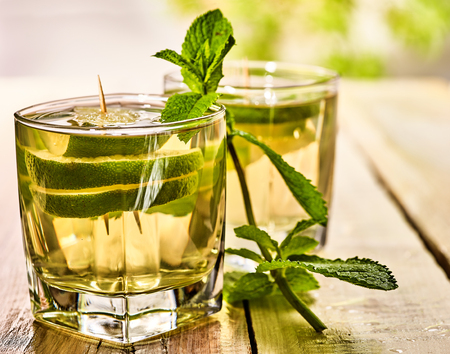 Alcohol drink. On wooden boards are two glasses with alcohol green transparent drink. A drink number seventeen mojito cocktail with lime and mint leaf . Country life. Light background.の写真素材