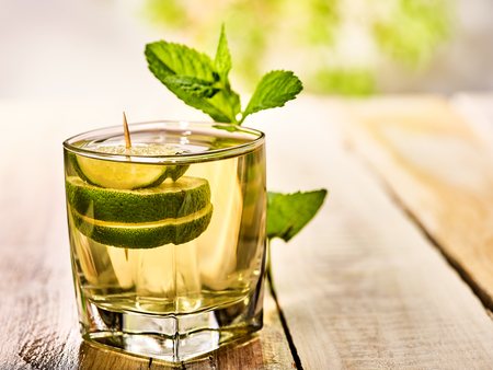 Alcohol drink. On wooden boards is glass with alcohol green transparent drink. A drink number twelwe cocktail mohito with slice lime and mint leaf. Country life. Outdoor. Light background.の写真素材