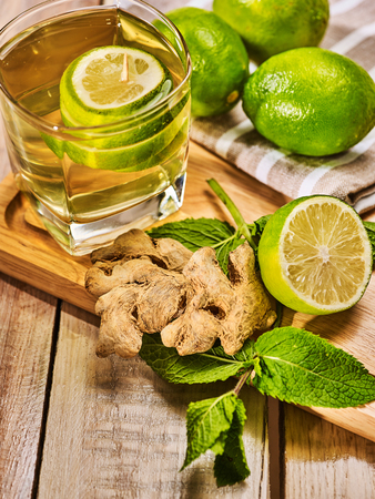 Healthy detox drink with ginger . On wooden boards glass with green tea and mint. A mint ginger drink number twenty five with half lime and napkin. Country life. Light background.の写真素材