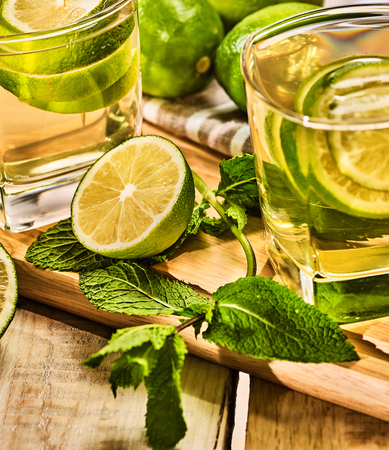 Alcohol drink. On wooden board couple of glasses with alcohol green mohito drink. A mint drink number twenty two mojito cocktail with half lime and napkin. Country life. Light background.の写真素材