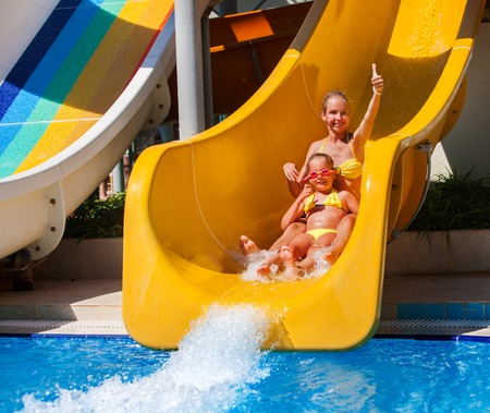 Two children on water slide at aquapark and thumb up. Summer holiday. There are two water slides in aqua park. There many slidees outdoor.の写真素材