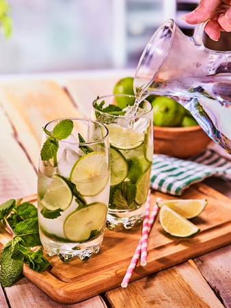 Country drink. Hand is pouring from jug of cocktail drink on wooden boards with lime and mint . Drink number forty with mohito cocktail and ice cubes . Country life. Light background.の写真素材