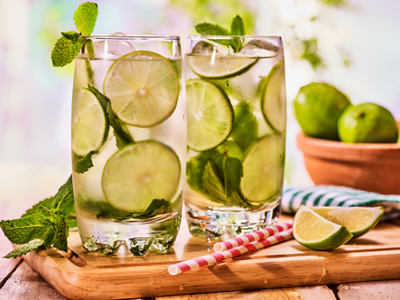 Alcohol drink. On wooden boards two glasses with alcohol drink and ice cubes. A drink number thirty three cocktail mohito with straw and lime and mint leaf. Country life. Outdoor. Light background.の写真素材