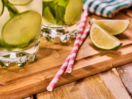 Alcohol drink. On wooden boards part of two glasses with alcohol drink and ice cubes. A drink number forty two cocktail mohito with straw and lime and mint leaf. Country life. Light background.の写真素材