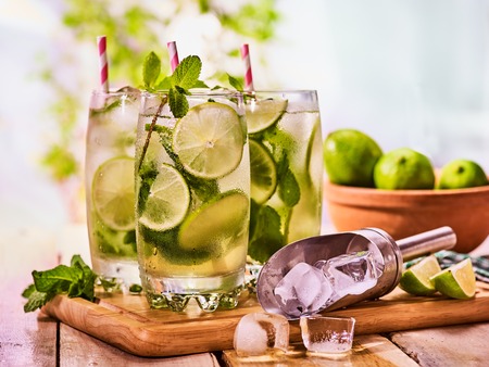 Alcohol drink. On wooden boards three glasses with alcohol drink and ice cubes. A drink number thirty six cocktail mohito and scoop ice with straw. Country life. Outdoor. Light background.の写真素材