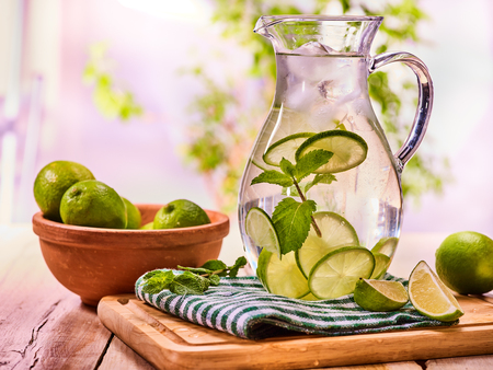 Country drink. On wooden boards is glass jug with transparent drink and lime glue bowl. A drink number thirty one with ice cubes . Country life. Light background.の写真素材
