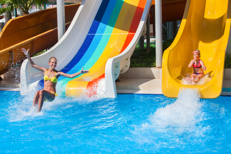 Two children sisters on water slide at aquapark shows thumb up. Summer holiday. There are two water slides in aqua park. Outdoor.の写真素材
