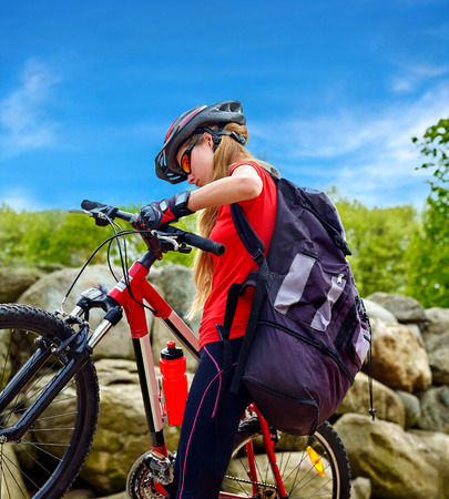 Bikes bicyclist girl. Girl rides bicycle into mountains. Girl on bicycle in mountaineering . Girl carries her bike over rocks. Bicyclist looks at his feet aganist blue sky.の写真素材