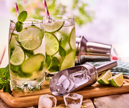 Alcohol drink. On wooden boards two glasses with alcohol drink and ice cubes. A drink number seventy four cocktail mohito and scoop ice and cocktail shaker . Country life. Outdoor. Light background.の写真素材