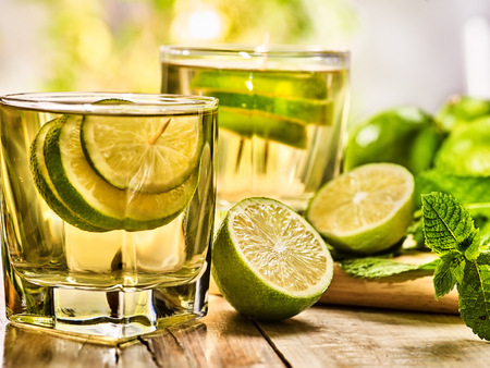 Alcohol drink. On wooden boards two glasses with alcohol green transparent drink and half lime . Drink number seventy one cocktail mojito with slice lime and mint leaf. Country life. Light background.の写真素材