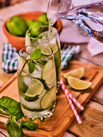 Country drink. Pouring from jug of cocktail drink on wooden boards with lime and mint . Drink number seventy three with mohito cocktail and ice cubes . Country life. Light background.の写真素材
