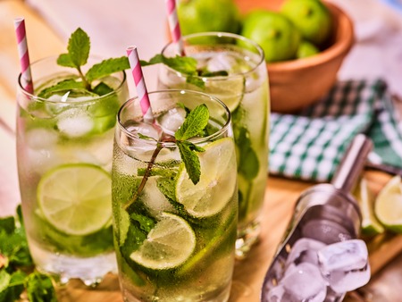 Alcohol drink. On wooden boards three glasses with alcohol drink and ice cubes. A drink number seventy five cocktail mohito and scoop ice with straw. Country life. Outdoor. Light background.の写真素材