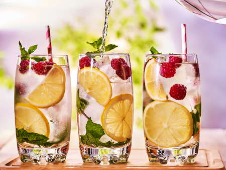 On wooden boards are three cocktail glasses with berries lemon and ice cubes. Pouring alcohol country cocktail number eighty eight. Garden outdoor.の写真素材