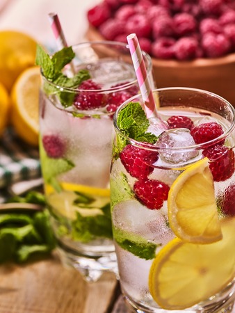 On wooden boards is cocktail glass with berries lemon and ice cubes. Alcohol country cocktail number ninety two with clay bowl raspberries with mint and ice cubes. Country life cocktail.の写真素材