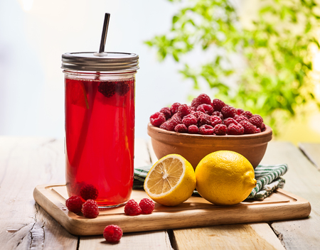 On wooden boards is ice cold drink glasses with raspberry lemon cocktail . Country ice cold drink number ninety three with raspberry clay bowl outdoor with green tree.の写真素材