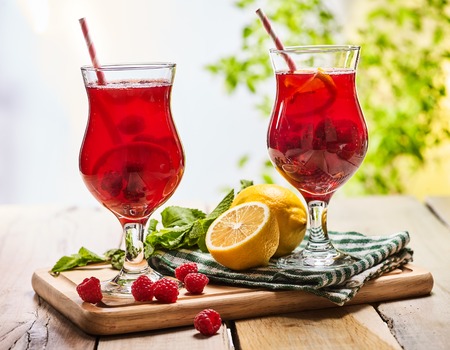 On wooden boards are ice cold beverage two glasses with red berries lemon cocktail . Alcohol country cocktail beverage number ninety seven with leaf mint. Outdoor cocktail .の写真素材