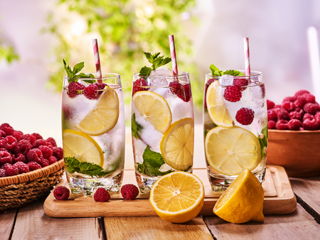 On wooden boards three glasses with ice cubes alcohol cocktail number hundred twenty two raspberry cocktail mohito with straw and lime and mint leaf. Country life. Outdoor. Light background.の写真素材