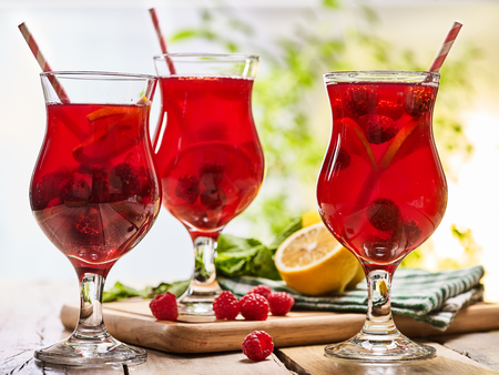 On wooden boards are ice cold beverage glasses with red raspberry lemon cocktail . Alcohol country cocktail beverage number hundred thirty two with drinking straw. Cocktail on outdoor.の写真素材