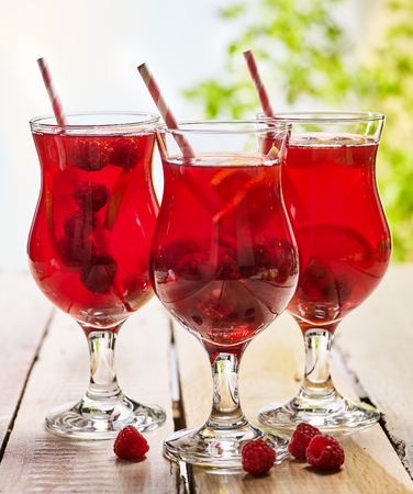 On wooden boards are ice cold beverage glasses with red raspberry lemon cocktail . Alcohol country cocktail beverage number hundred thirty three with raspberry . Cocktail on outdoor corporate.の写真素材