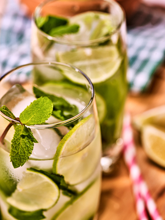 Alcohol drink. On wooden boards part of two glasses with lime alcohol drink and ice cubes. A drink number hundred eleven with two straw cocktails mohito and mint leaf. Country life. Light background.の写真素材