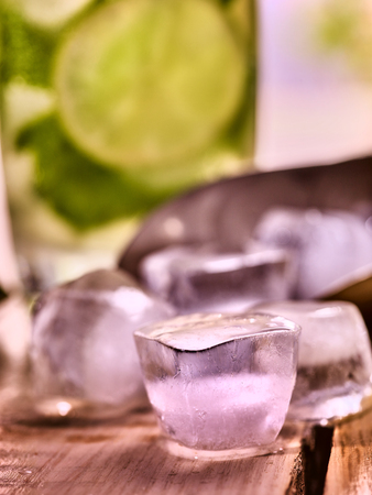 Chunks of ice cubes alcohol drink background on wooden boards. A drink number hundred nine cocktail mohito with slice lime and mint leaf.の写真素材