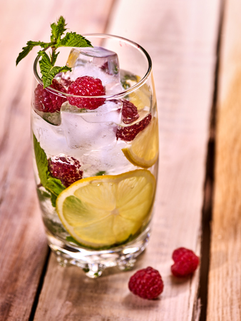 Alcohol drink. On wooden boards is glass with alcohol drink and ice cubes. A drink number hundred sixteen cocktail raspberry mojito with slice lime and mint leaf. Country life. Light background.の写真素材