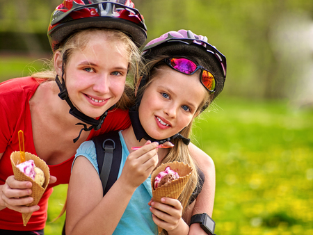 Bikes bicyclist girl. Girls wearing bicycle helmet with rucksack rides bicycle in summer park. Happy girls biking eating ice cream cone . Bicyclist is looking at camera.の写真素材