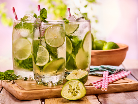 Alcohol drink. On wooden boards three glasses with ice cubes alcohol drink . A drink number hundred fourteen cocktail mohito with straw and lime and mint leaf. Country life. Outdoor. Light background.の写真素材