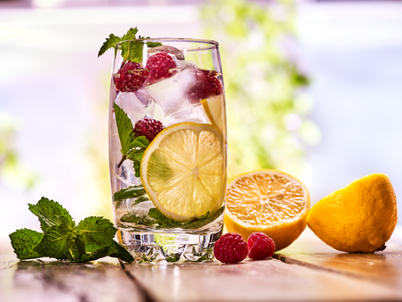 Alcohol drink. On wooden boards is glass with alcohol drink and ice cubes. A drink number hundred seventeen cocktail raspberry mojito and half lime with mint. Country life. Outdoor. Light background.の写真素材