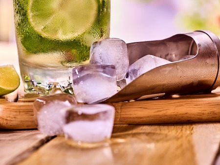 Chunks of ice cubes alcohol drink background on wooden boards. Part of drink number two hundred fifty four cocktail mohito with slice lime and mint leaf.の写真素材