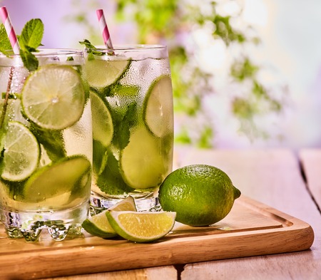 Alcohol drink. Wooden boards three glasses with green alcohol cocktail drink and ice cubes. Drink three hundred and ten cocktail mohito and cube ice with striped straw. Country life. Light background.の写真素材