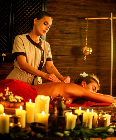 Young woman lying on luxary wooden spa bed. Massage in spa salon with masseuse . A lot of candles background in massage spa salon.の写真素材
