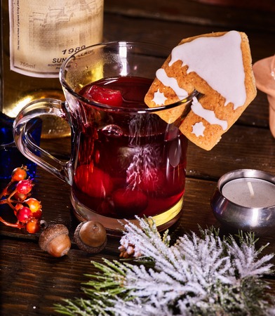 Close up of glass mug of warming smoking bishop drink with bottle of wine . Label on bottle of wine. Warming mulled wine with cookie in form of house on brick wall.の写真素材