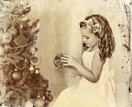 Child decorate on Christmas tree. Old photo on yellow paper. Child home alone.の写真素材