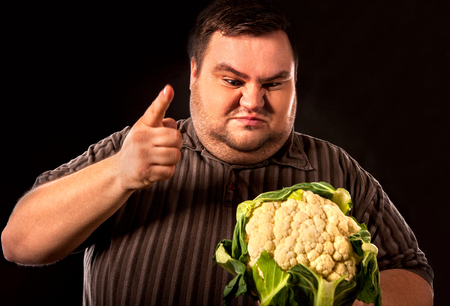 Diet fat man eating healthy food . Healthy breakfast with vegetables cauliflower for overweight person. Male trying to lose weight. Concept on black background.の写真素材