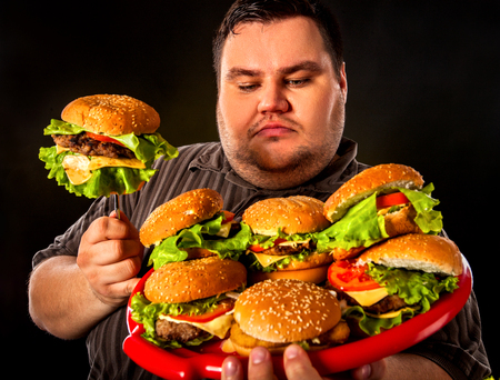Fat man eating fast food hamberger. Breakfast for overweight person. Junk meal leads to obesity. Person regularly overeats concept on black background.の写真素材