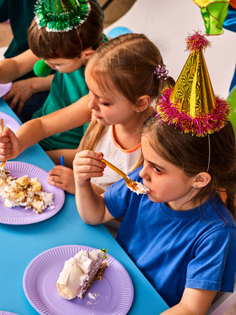 Birthday children celebrate party and eating cake on plate together . Portrait of three kids happy girl and boy in party hat sitting for table .の写真素材
