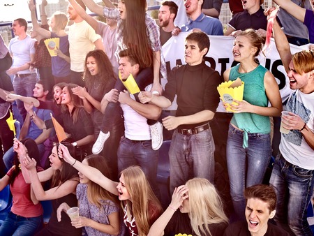 Fans cheering in stadium and eating popcorn in yellow boxes and drink beer. Group young people friends support your favorite team . Close up.の写真素材
