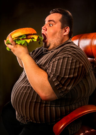 Diet failure of fat man eating fast food hamberger. Happy smile overweight person who spoiled healthy food by eating huge hamburger on fork. Junk meal leads to obesity. Very fat man eating fast food.の写真素材