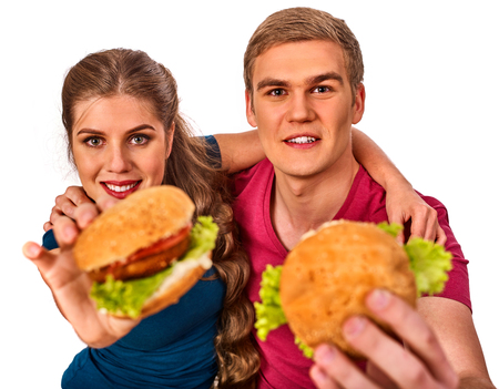 Couple eating fast food. Man and woman treat big hamburger with ham. Friends give burder junk on white background isolated. Beginner chefs and his food semi-finished products.の写真素材
